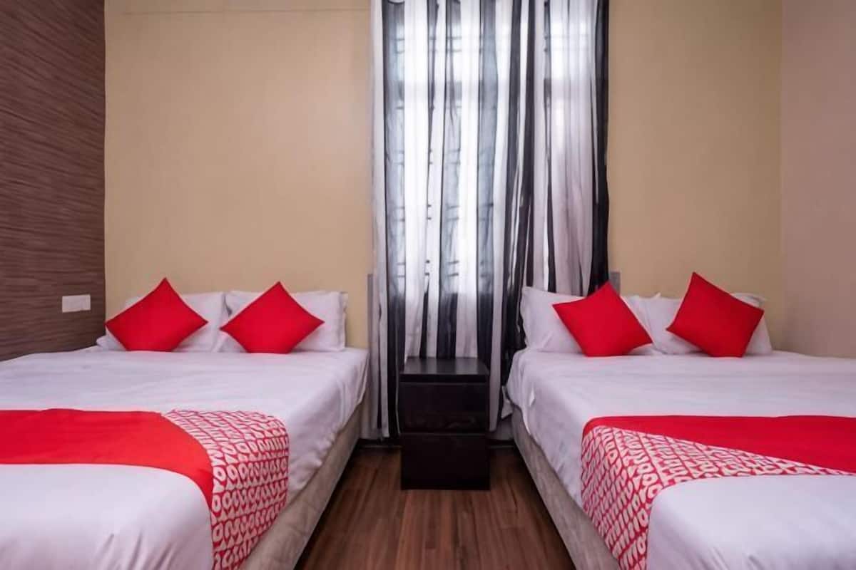 A hotel room with two beds, red and white bedding, a wooden floor, and a window with vertical blinds.