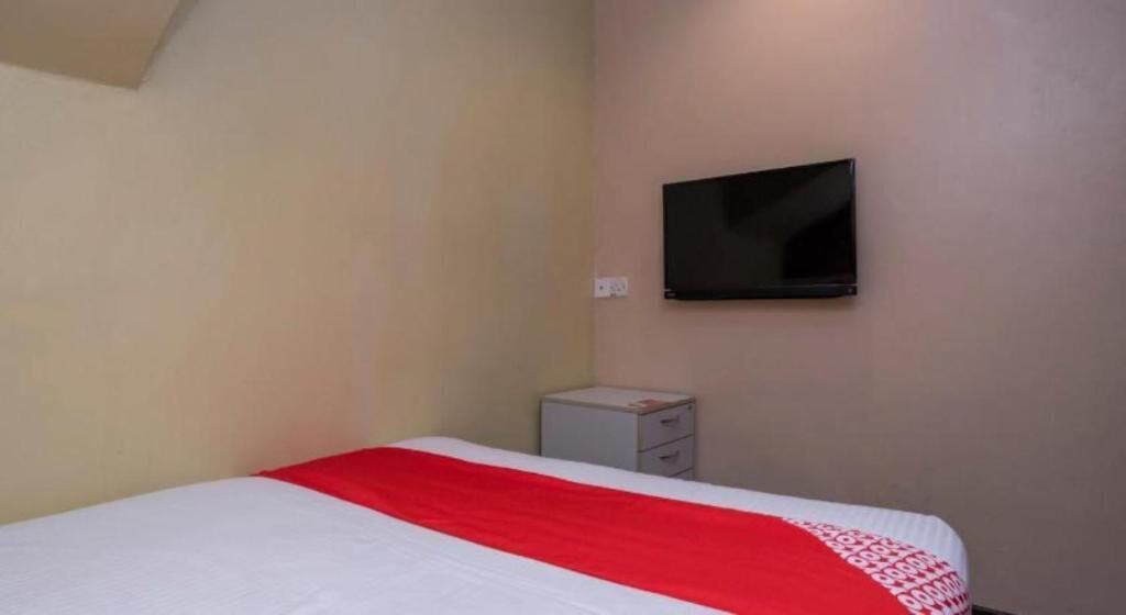 A hotel room with a bed, a television mounted on the wall, and a small bedside table.