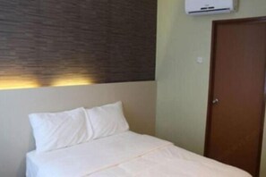Una cama individual con ropa de cama blanca en una habitación con pared texturizada y puerta de madera.
