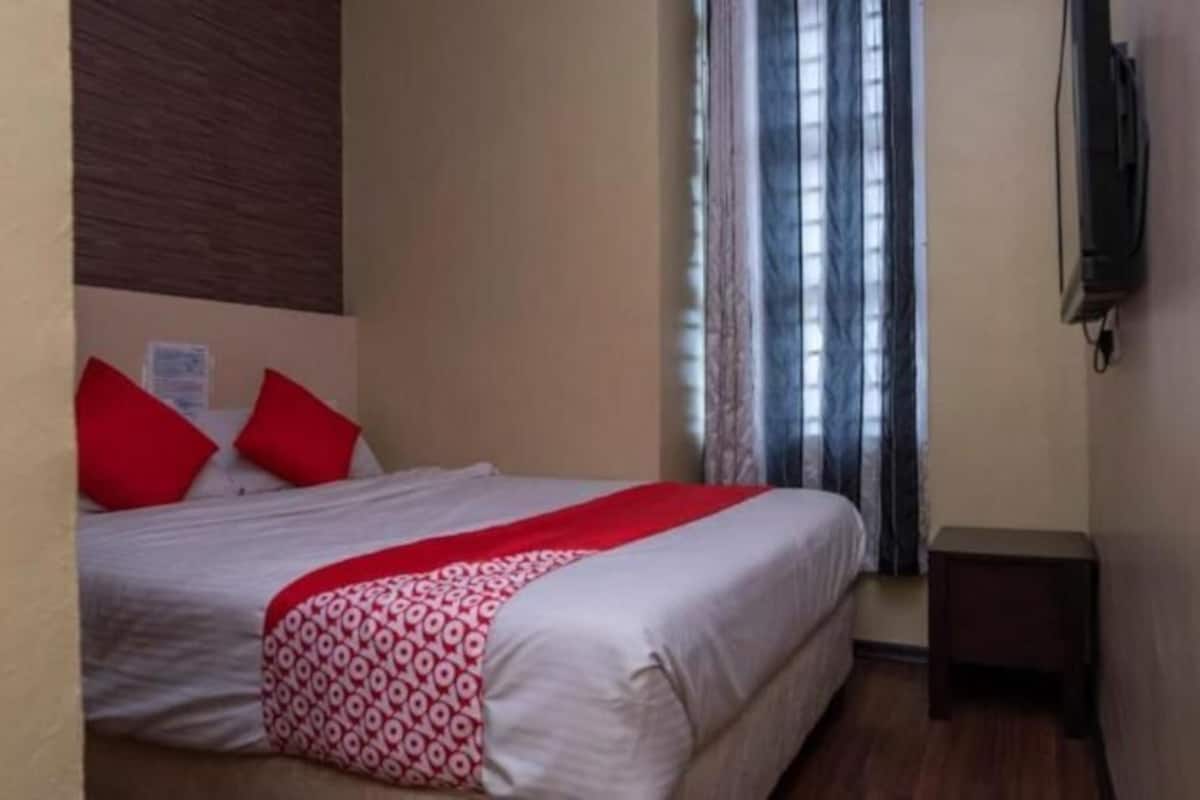 A hotel room with a bed, a small bedside table, and a TV mounted on the wall.