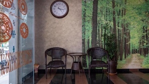 Una stanza con un affresco raffigurante una foresta, due poltrone in vimini, un tavolino rotondo e una sveglia a parete.
