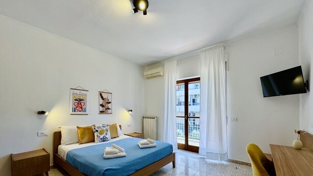 Une chambre à coucher avec un lit, un bureau, une chaise, une télévision et une fenêtre avec des rideaux.