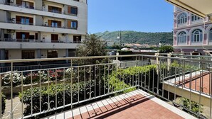 Un immeuble à plusieurs étages doté de balcons, d’une terrasse dallée et offrant une vue sur une colline.