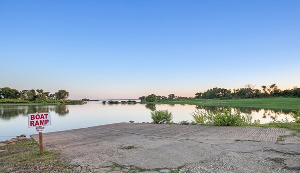 A boat ramp with a warning sign, a calm lake, and a grassy area with trees in the background.