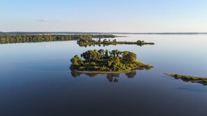 Ilmakuva pienestä, tiheästä metsästä peitetyistä saaresta, jonka ympärillä on tyyntä vettä.