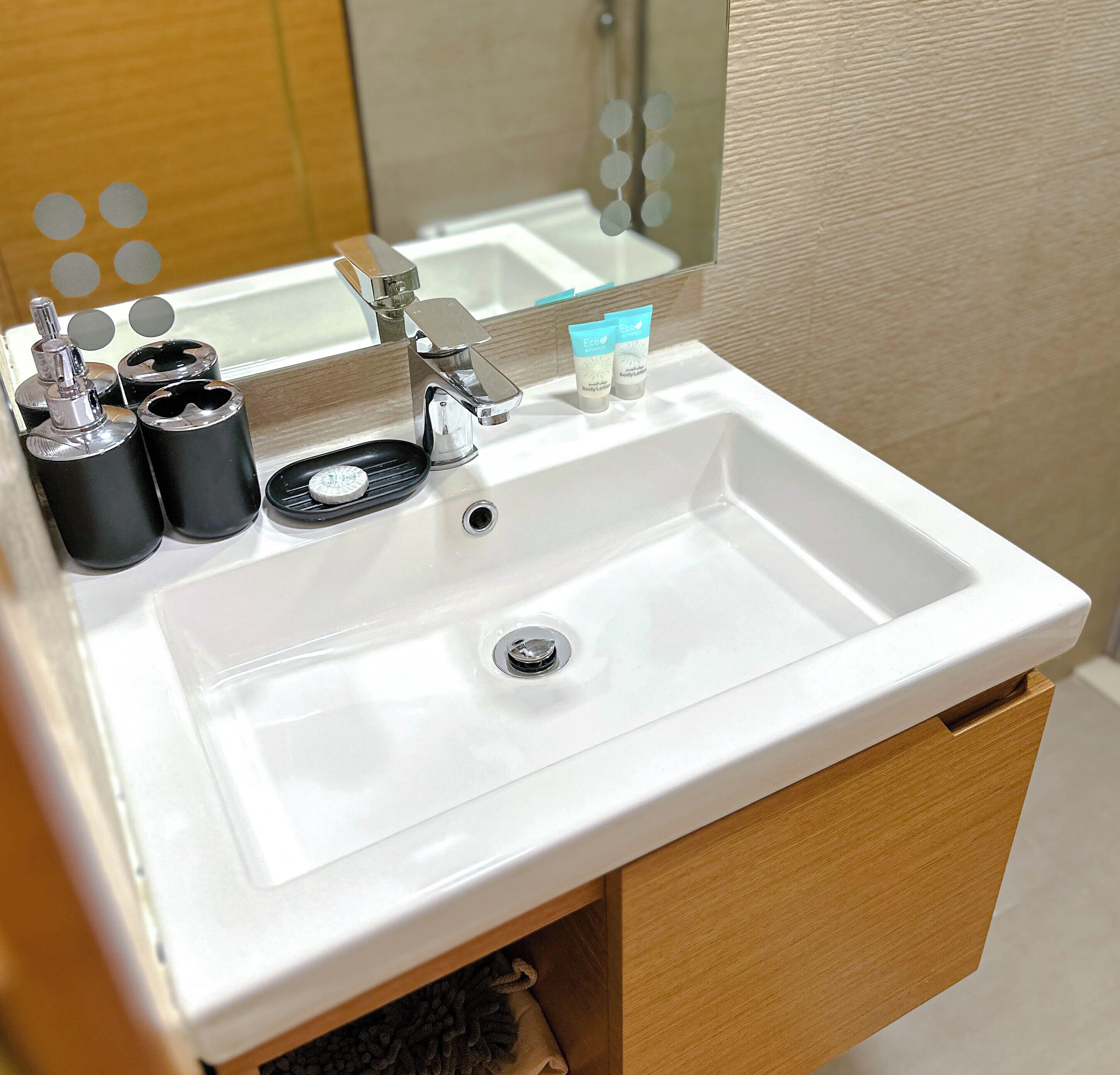 A white bathroom sink with a chrome faucet, two black soap dispensers, and a small mirror above the sink.