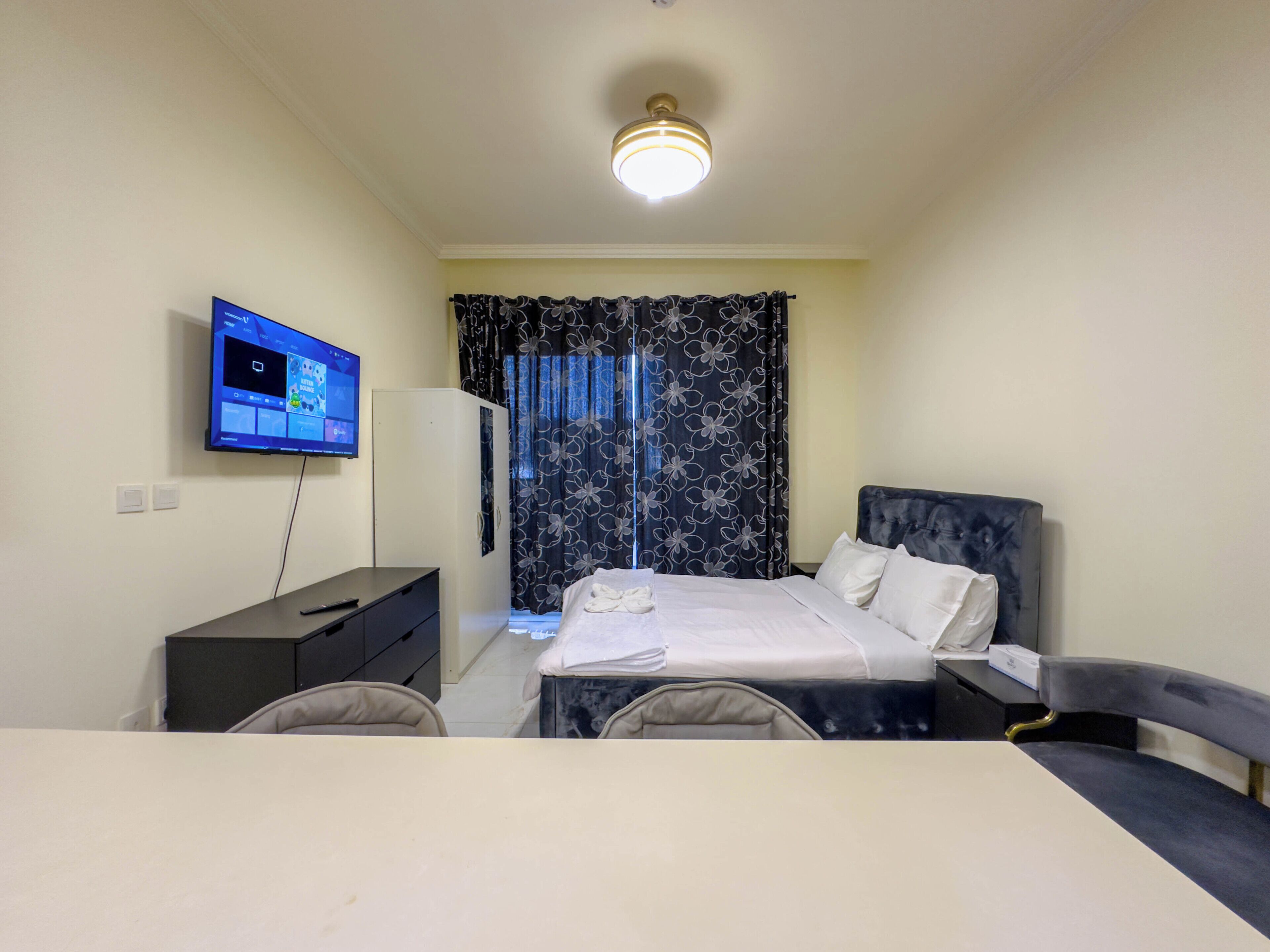 A hotel room with a bed, a desk with a chair, a television, and a wardrobe.