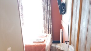 Een hotelkamer met een bed, een klein krukje, een houten deur en een raam met gordijnen.