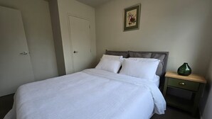 Ein ordentlich bezogenes Bett mit weißen Leinen in einem Zimmer, dessen Tür geschlossen ist, und ein kleiner Nachttisch mit einer grünen Vase.