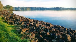 Eine felsige Küstenlinie mit ruhigem Wasser und einer entfernten Ansicht einer Stadt am gegenüberliegenden Ufer.