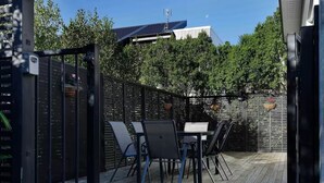Eine Terrasse im Freien mit Tisch und Stühlen, umgeben von einem Holzboden und einem Metallzaun.