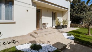 Une maison moderne à deux étages, dotée d’un toit plat, d’un porche abrité et d’un petit espace extérieur aménagé pour s’asseoir.