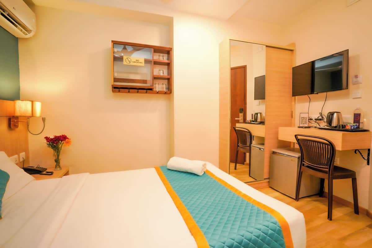A hotel room with a bed, a desk, a chair, a TV, and a small kitchenette.