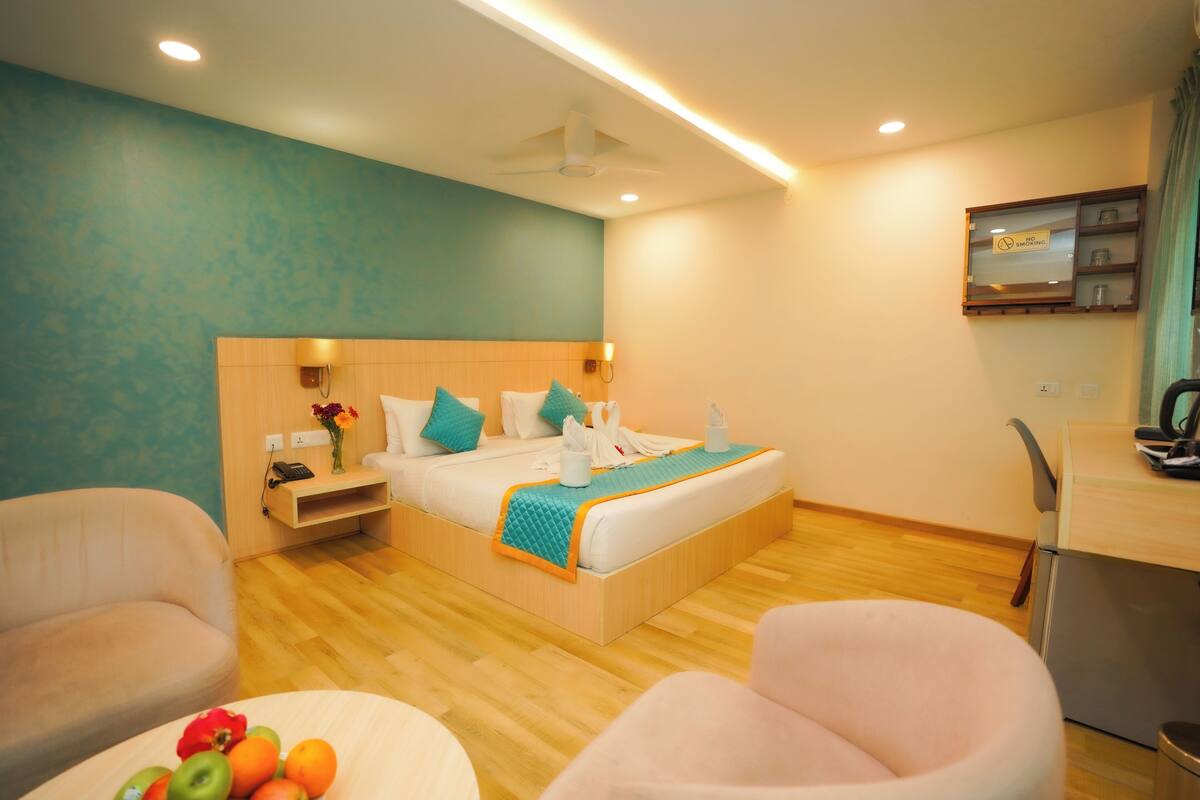 A modern hotel room with a bed, a desk, a chair, and a small table with fruit.
