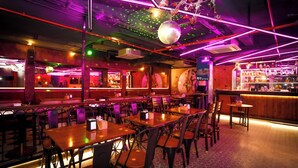 A restaurant with tables and chairs, a bar area, and decorative lighting. - Santrina Hotels (Bengaluru)