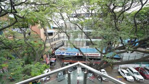A view from a balcony overlooking a street with parked cars and a restaurant with a blue roof. - Santrina Hotels (Bengaluru)