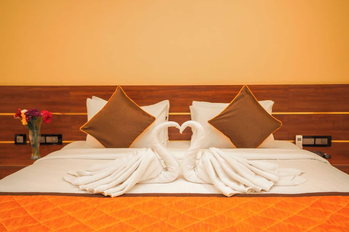 A hotel room with a bed featuring a heart-shaped towel arrangement and two pillows.
