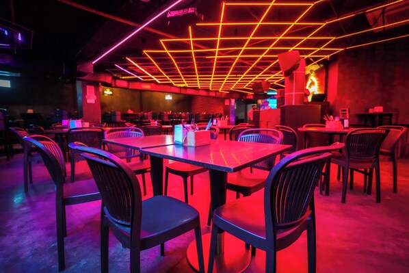 A restaurant with multiple tables and chairs, neon ceiling lights, and a modern interior design. - Santrina Hotels (Bengaluru)
