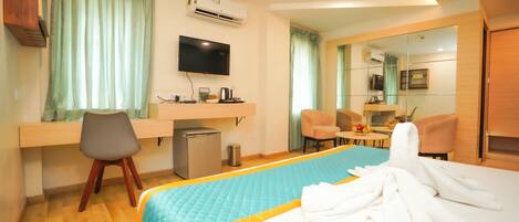 Ein Hotelzimmer mit Bett, Schreibtisch, Stuhl, Fernseher und einer kleinen Küchenzeile.