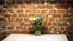 Eine Vase mit Blumen auf einem Tisch vor einer Ziegelwand.