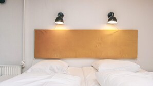 Ein Hotelzimmer mit einem hölzernen Kopfteil, zwei Nachttischlampen und weißer Bettwäsche.