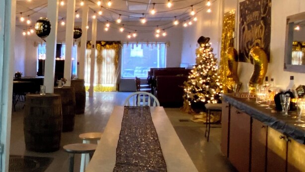 Um espaço interior acolhedor, com área de bar central, árvore de Natal e luzes penduradas no teto.