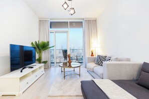 A modern living room with a flat-screen TV, a sofa, a coffee table, and a view of a cityscape through large windows. - Bloomfields Spacious 1BR Bloom Tower  (Dubai)