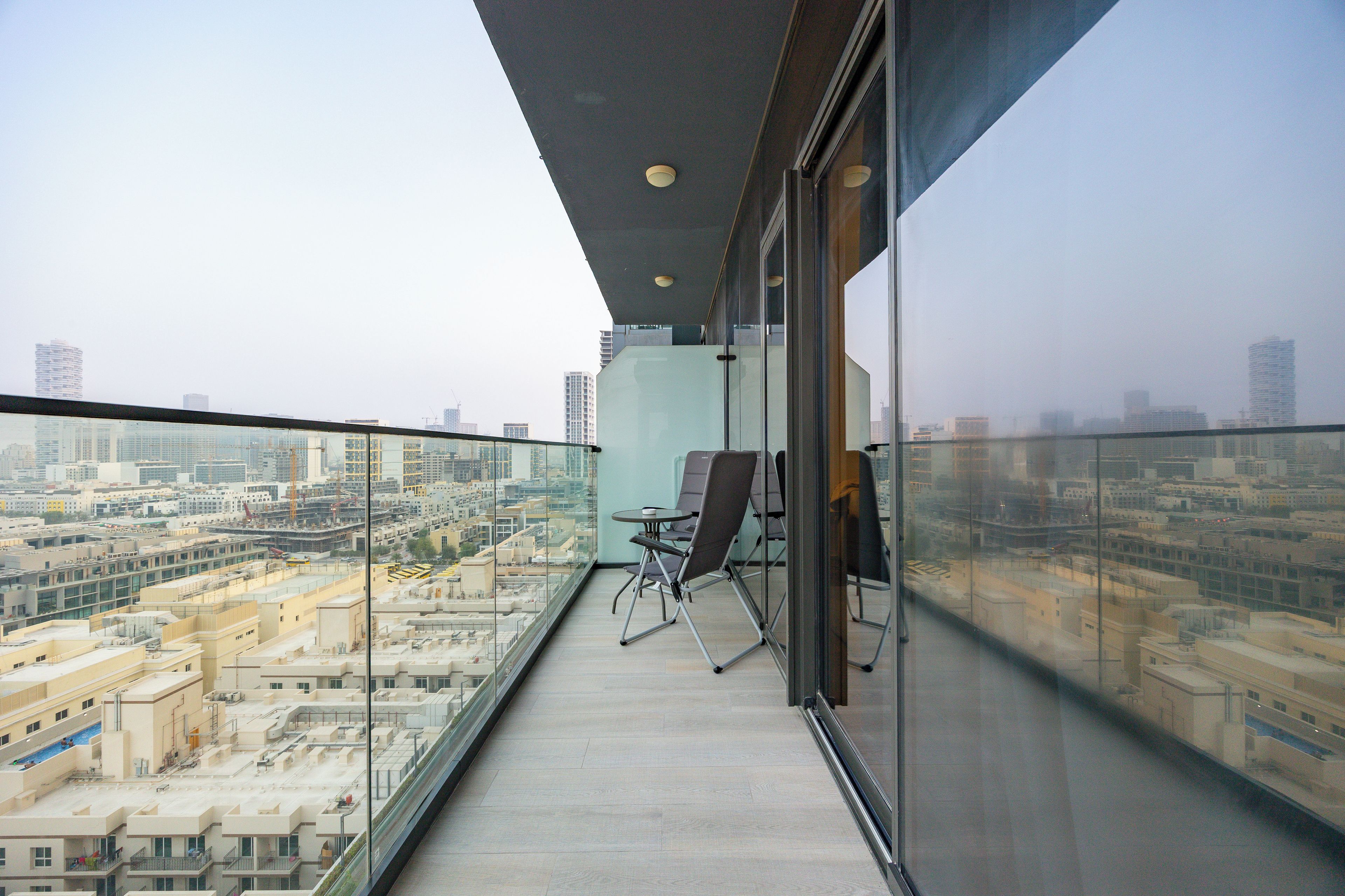 Un balcon donnant sur un paysage urbain, une paroi en verre et un fauteuil.