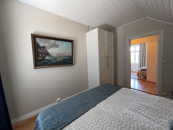 A bedroom with a bed, a wardrobe, a painting, and a door leading to another room.