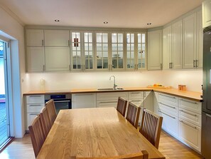 A modern kitchen with white cabinets, a wooden dining table, and a built-in oven.