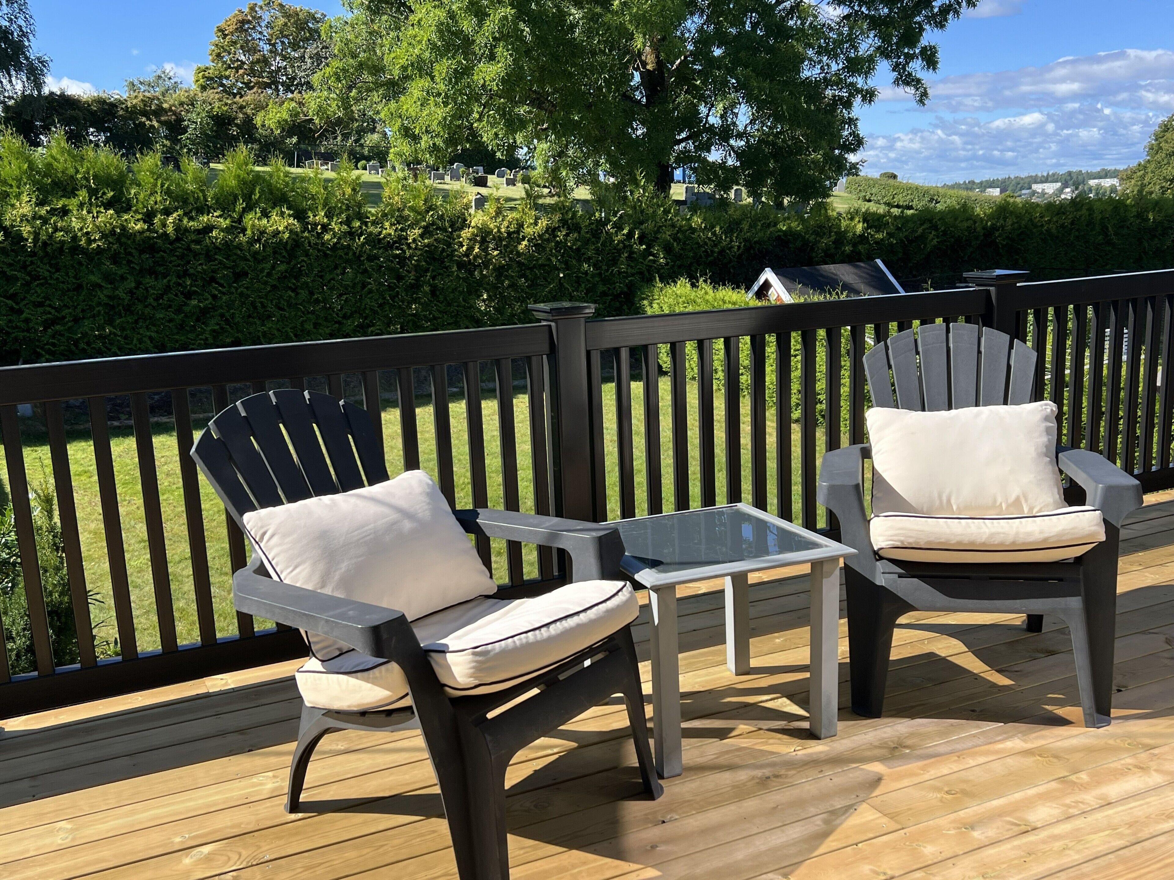 Une terrasse avec deux chaises Adirondack et une petite table, entourée d’une autre terrasse en bois et d’une rambarde noire.