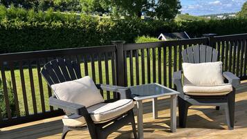 Une terrasse avec deux chaises Adirondack et une petite table, entourée d’une autre terrasse en bois et d’une rambarde noire.