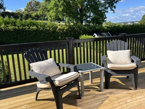 Une terrasse avec deux chaises Adirondack et une petite table, entourée d’une autre terrasse en bois et d’une rambarde noire.