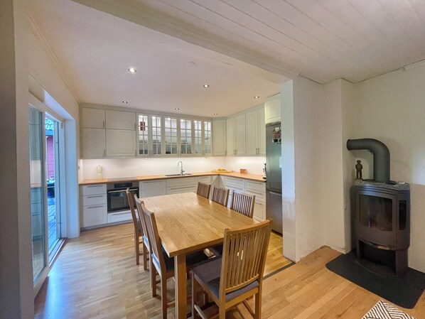 A modern kitchen with a dining area, wooden flooring, and a built-in wood stove.