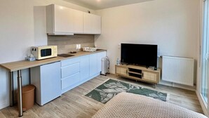 Eine moderne Küche mit weißen Schränken, einer Mikrowelle und einem Fernseher auf einem Holzboden.