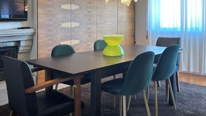 Een moderne eetruimte met een houten accentmuur, een felgele tafellamp en blauwgroene stoelen.
