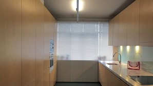 Een moderne keuken met houten kastjes, een zwart aanrecht en een raam met zonwering.