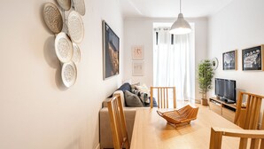 A modern living room with a dining table, wooden chairs, a sofa, a TV, and wall art. - Carob Apartment, Baixa, Lisbon (Lisboa)