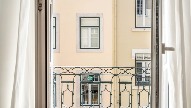 A view through a window with a metal balcony railing, a building with multiple windows, and a door. - Carob Apartment, Baixa, Lisbon (Lisboa)