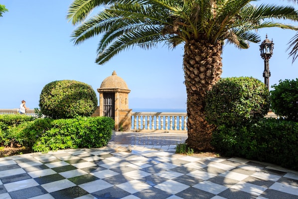 A checkered pathway leading to a building with a dome, surrounded by lush greenery and a palm tree. - Apartment with patio in Cádiz downtown (Cadiz)