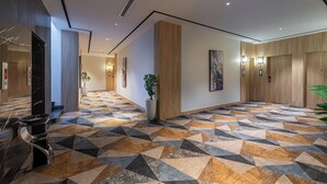 A modern hotel lobby with a geometric patterned floor, a reception desk, a potted plant, and artwork on the walls. - Al Qasr Hotel Taif (Taif)