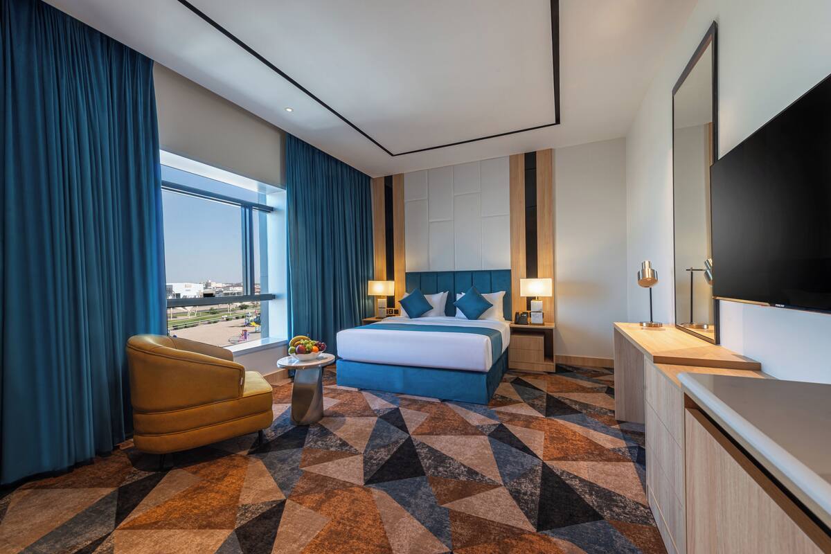 A hotel room with a large bed, a desk, a chair, and a view of the city.