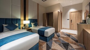 A hotel room with two beds, a nightstand with a lamp, a wardrobe, and a desk with a vase. - Al Qasr Hotel Taif (Taif)