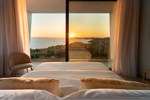 Un dormitorio con una cama grande, una silla y vistas al océano al atardecer.