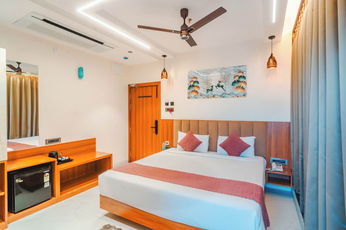 A hotel room with a bed, a desk, a refrigerator, a ceiling fan, and a painting on the wall.