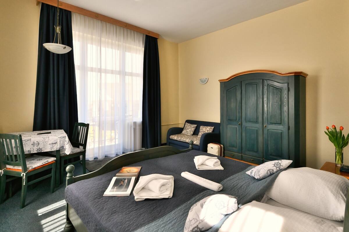 Une chambre d’hôtel comprenant un lit, un bureau avec une chaise, une armoire et une fenêtre avec des rideaux.