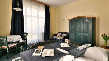 A hotel room with a bed, a desk with a chair, a wardrobe, and a window with curtains.