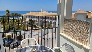 Un balcón con vista al mar, una mesa con sillas y un cerramiento de celosía.