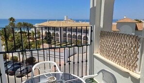 Un balcón con vista al mar, una mesa con sillas y un cerramiento de celosía.