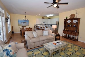 A living room with a sofa, coffee table, and a dining area with chairs. - 79 Ocean Creek (Fripp Island)